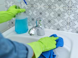 Woman in gloves with rag doing cleaning in bathroom, wash and polish washbasin and chrome-plated faucet